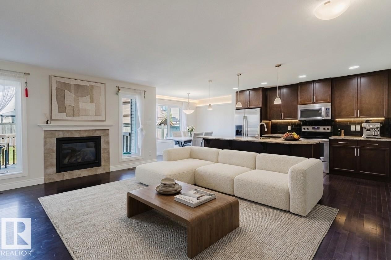 Open-concept living space featuring wood-finish flooring, a tiled fireplace, and multiple windows - 17348 6 Avenue Sw, Edmonton, AB - Indoor Photo Showing Living Room With Fireplace