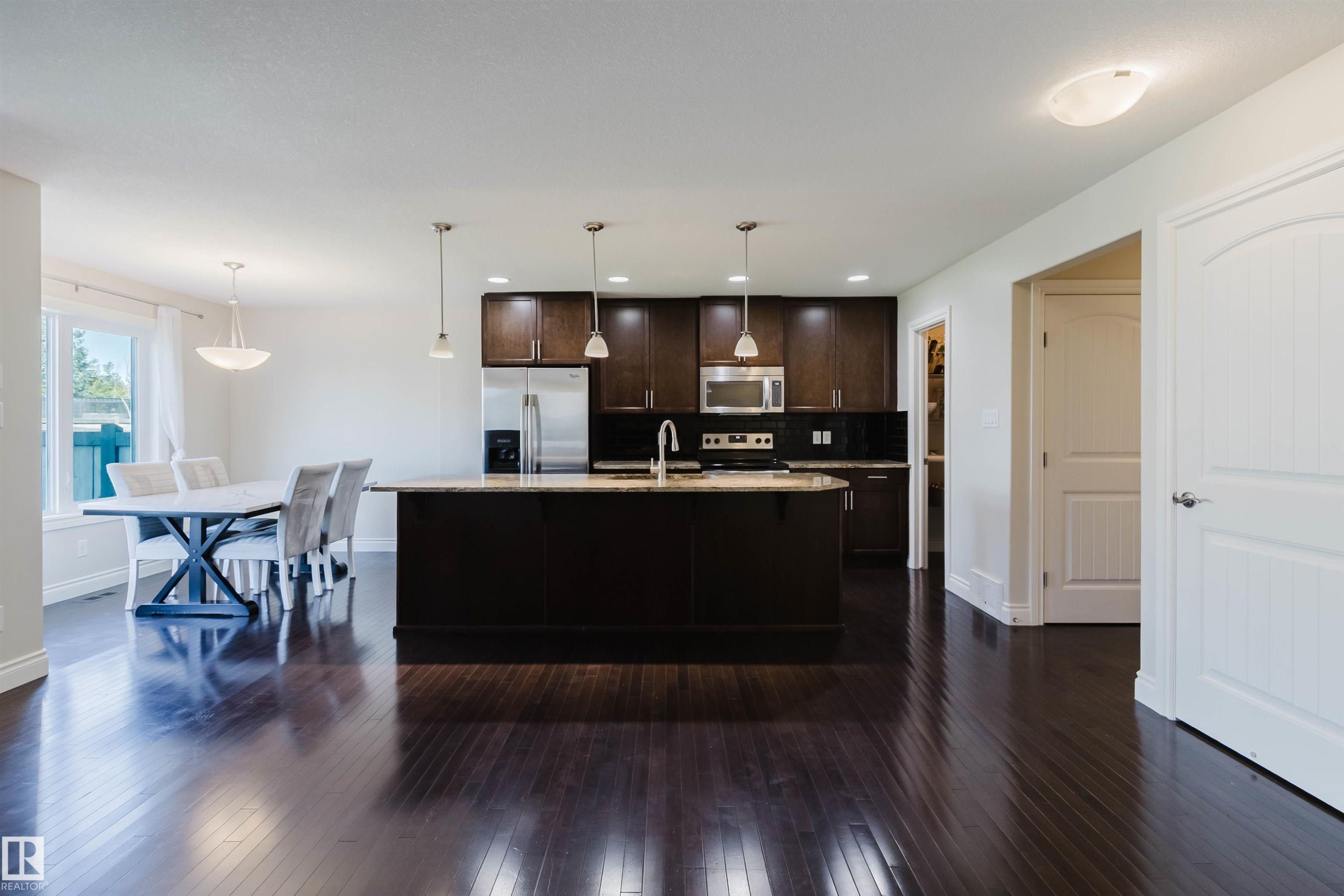 Open-concept kitchen and dining area featuring dark wood-finish flooring, a kitchen island with pendant lighting, stainless steel appliances, dark cabinetry, and white interior doors - 17348 6 Avenue Sw, Edmonton, AB - Indoor Photo Showing Other Room