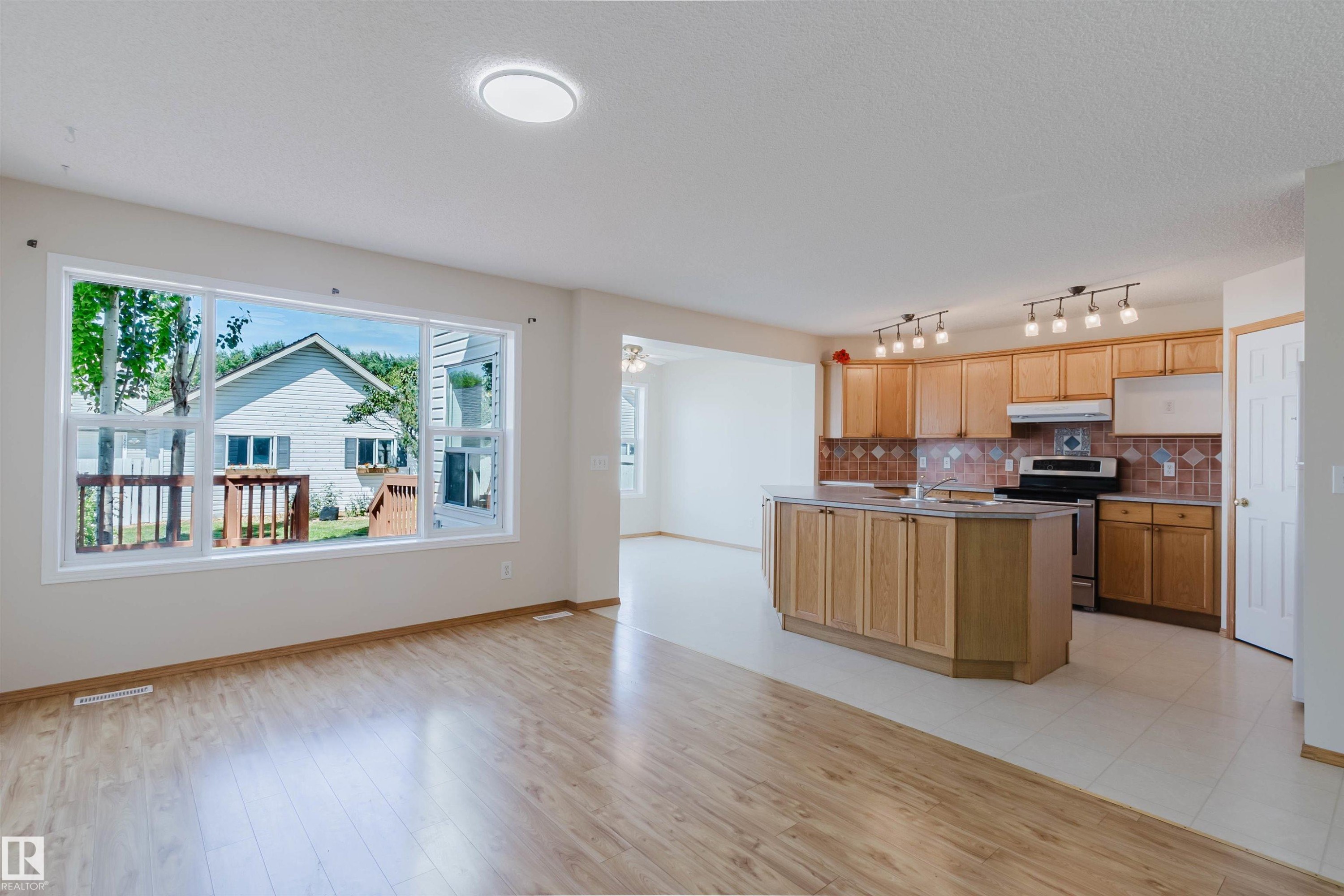 Open-concept interior featuring wood-finish flooring, a spacious kitchen island, extensive wood cabinetry, and a full tile backsplash - 1686 Tompkins Wynd Nw, Edmonton, AB - Indoor