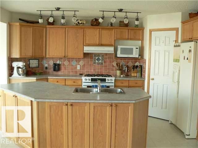 Kitchen featuring an island with double sinks, light wood-finish cabinetry, track lighting, a tiled backsplash, and light-colored countertops - 1686 Tompkins Wynd Nw, Edmonton, AB - Indoor Photo Showing Kitchen