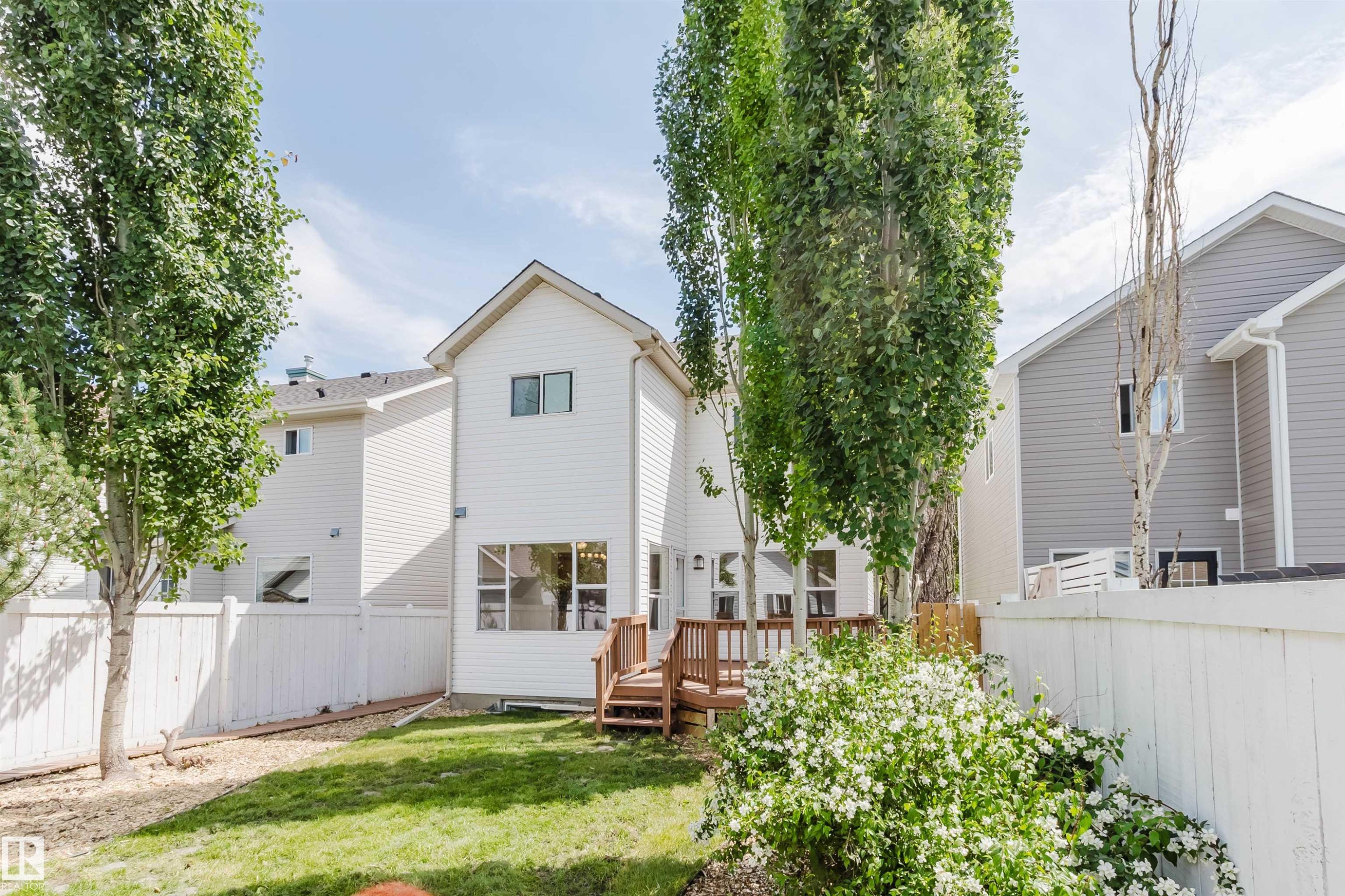 White siding exterior featuring a multi-level wood deck, a manicured lawn, and mature trees - 1686 Tompkins Wynd Nw, Edmonton, AB - Outdoor