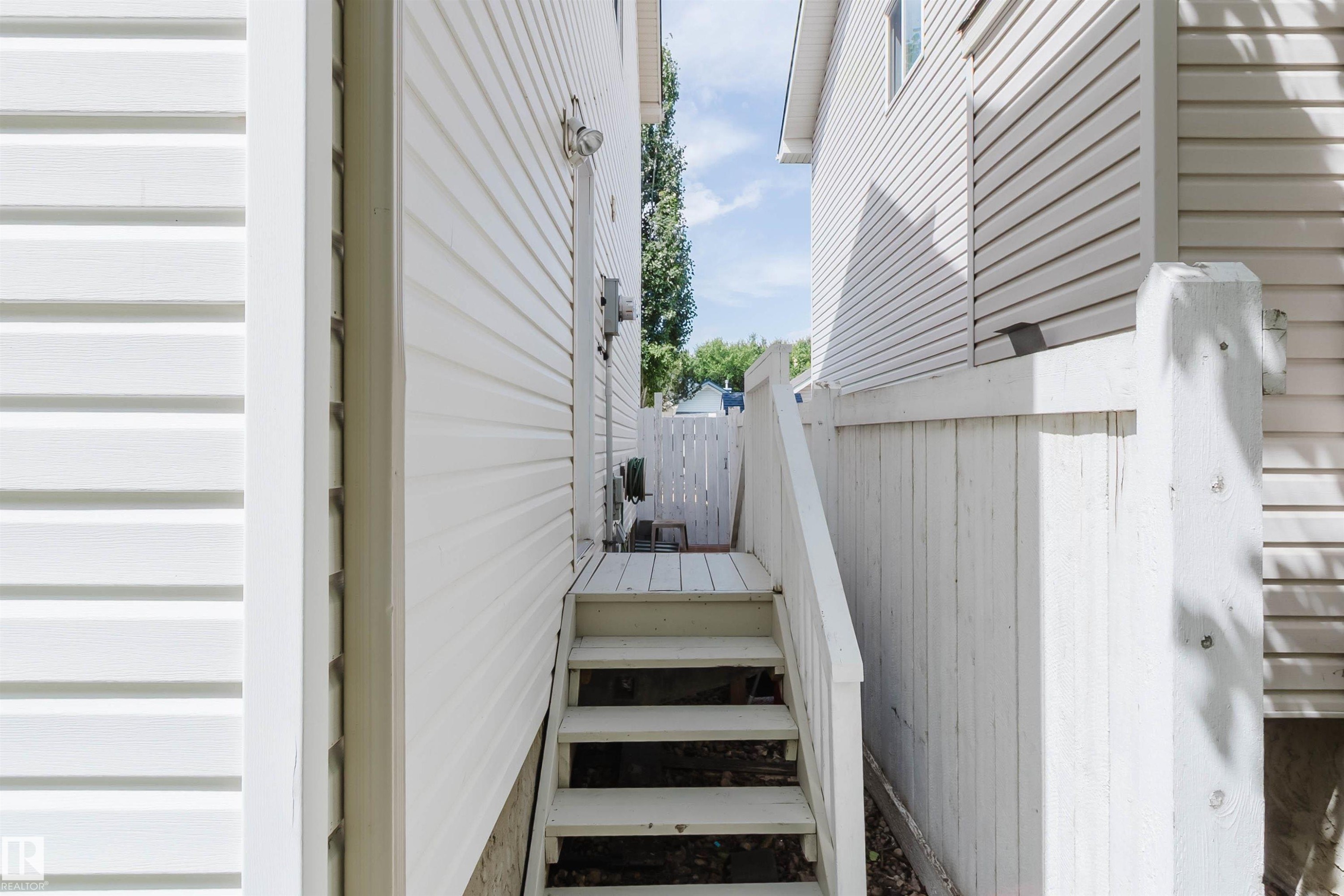 Exterior passageway featuring painted wood stairs, painted wood privacy fence, and white vinyl siding - 1686 Tompkins Wynd Nw, Edmonton, AB - Outdoor With Exterior