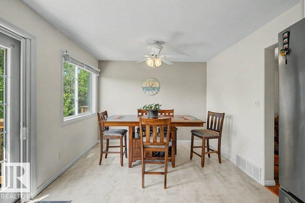Dining area featuring light-toned walls, a large window, a ceiling fan with integrated lighting, and wood-finish flooring - #39 2419 133 Av Nw, Edmonton, AB - Indoor Photo Showing Dining Room