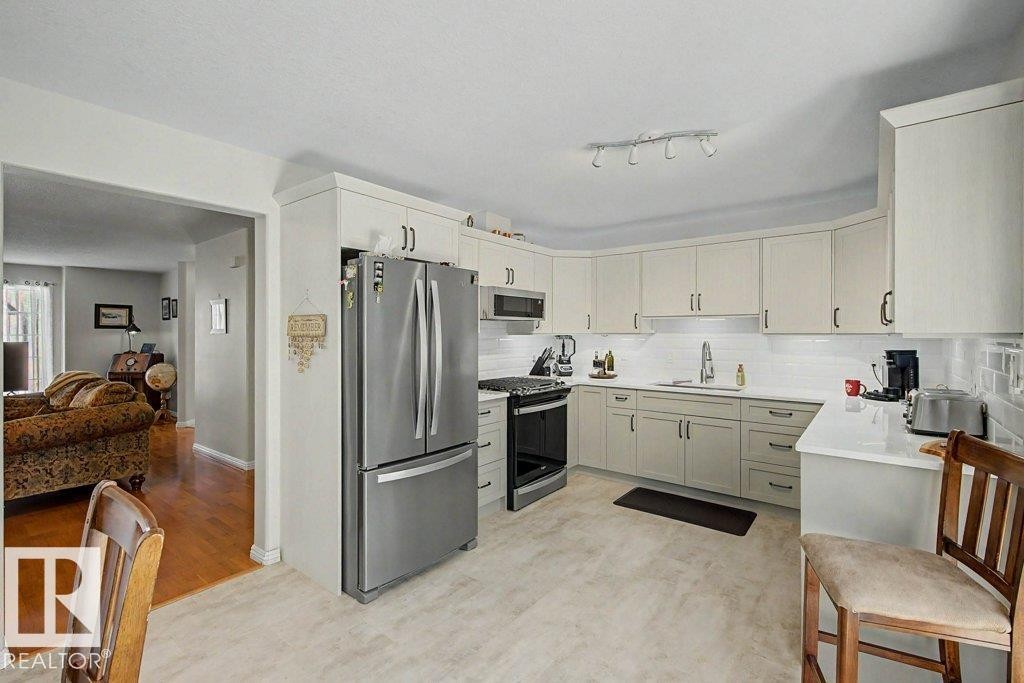 Kitchen featuring light-toned cabinetry with dark hardware, a stainless steel French door refrigerator, and a matching stainless steel range with an overhead microwave - #39 2419 133 Av Nw, Edmonton, AB - Indoor Photo Showing Kitchen