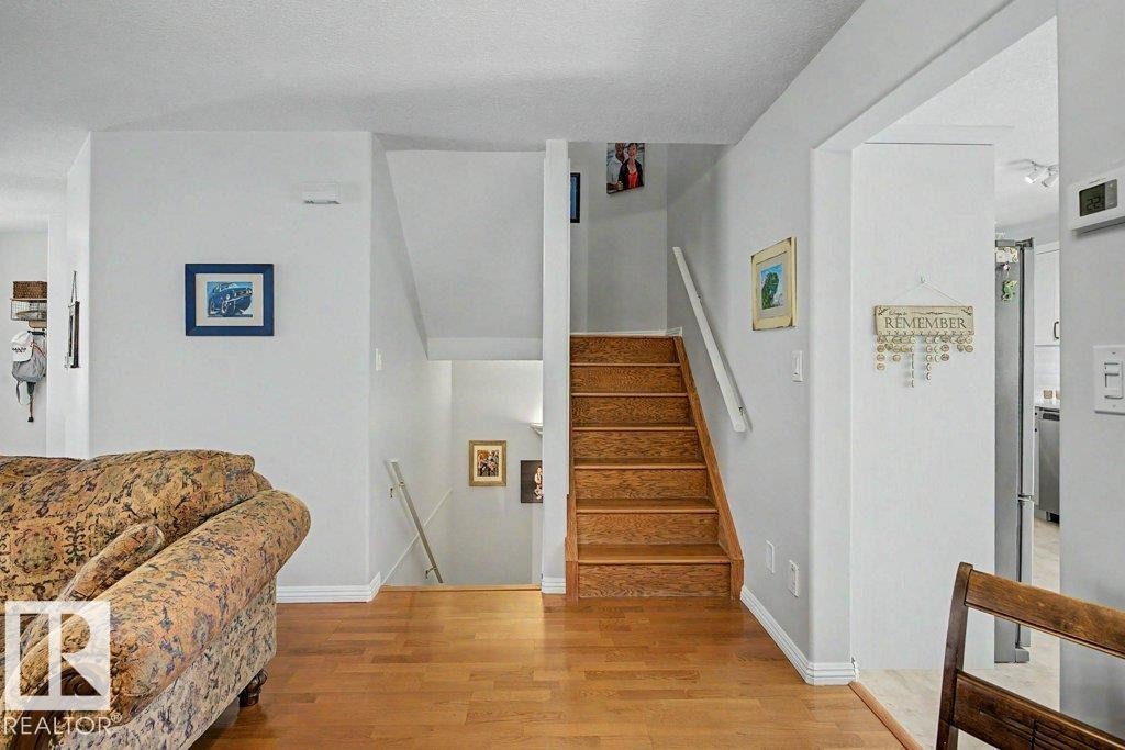 Wood-finish flooring throughout, bright white walls, and a multi-level staircase with wood treads and white risers - #39 2419 133 Av Nw, Edmonton, AB - Indoor