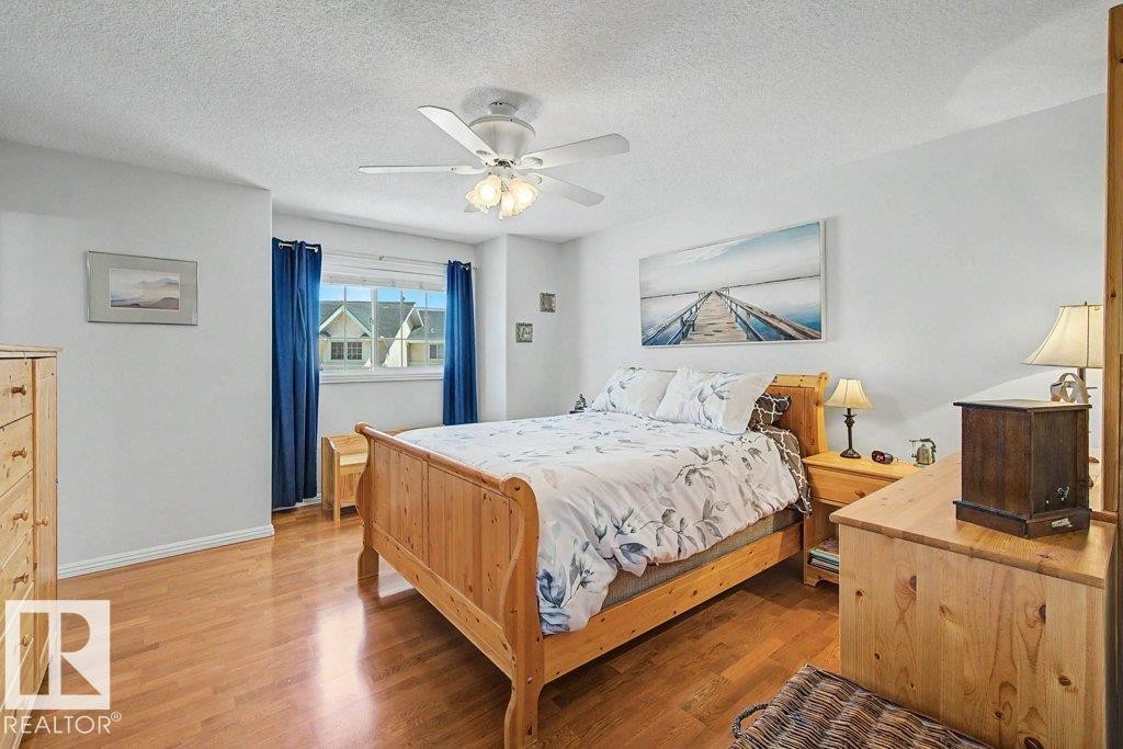 Hardwood-finish flooring, a white ceiling fan with integrated lighting, and a window with blue drapes - #39 2419 133 Av Nw, Edmonton, AB - Indoor Photo Showing Bedroom
