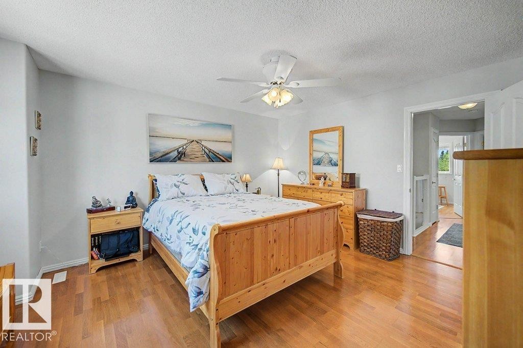 Bright bedroom featuring warm wood-finish flooring, light neutral wall paint, and a ceiling fan with integrated lighting - #39 2419 133 Av Nw, Edmonton, AB - Indoor Photo Showing Bedroom
