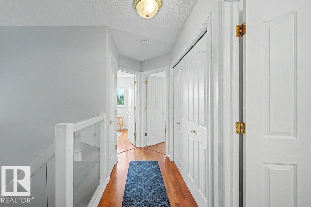 Hallway featuring wood-finish flooring, white panel doors with brass hardware, and a built-in display niche with glass shelving - #39 2419 133 Av Nw, Edmonton, AB - Indoor Photo Showing Other Room
