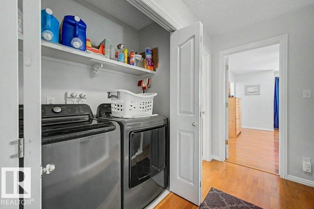 Dedicated laundry closet featuring a stacked washer and dryer, an overhead storage shelf, and a light gray wall finish - #39 2419 133 Av Nw, Edmonton, AB - Indoor Photo Showing Laundry Room