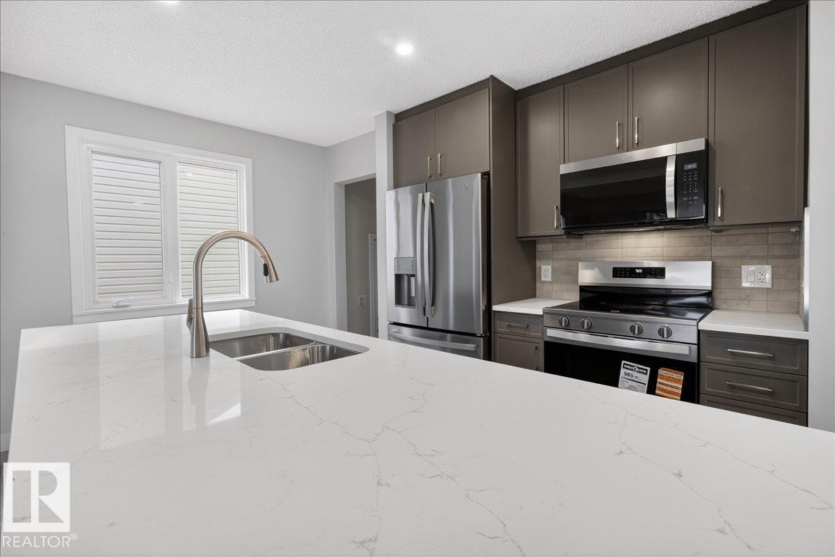 Kitchen featuring a large central island with a double stainless steel sink and a gooseneck faucet - 9723 65 Avenue Nw, Edmonton, AB