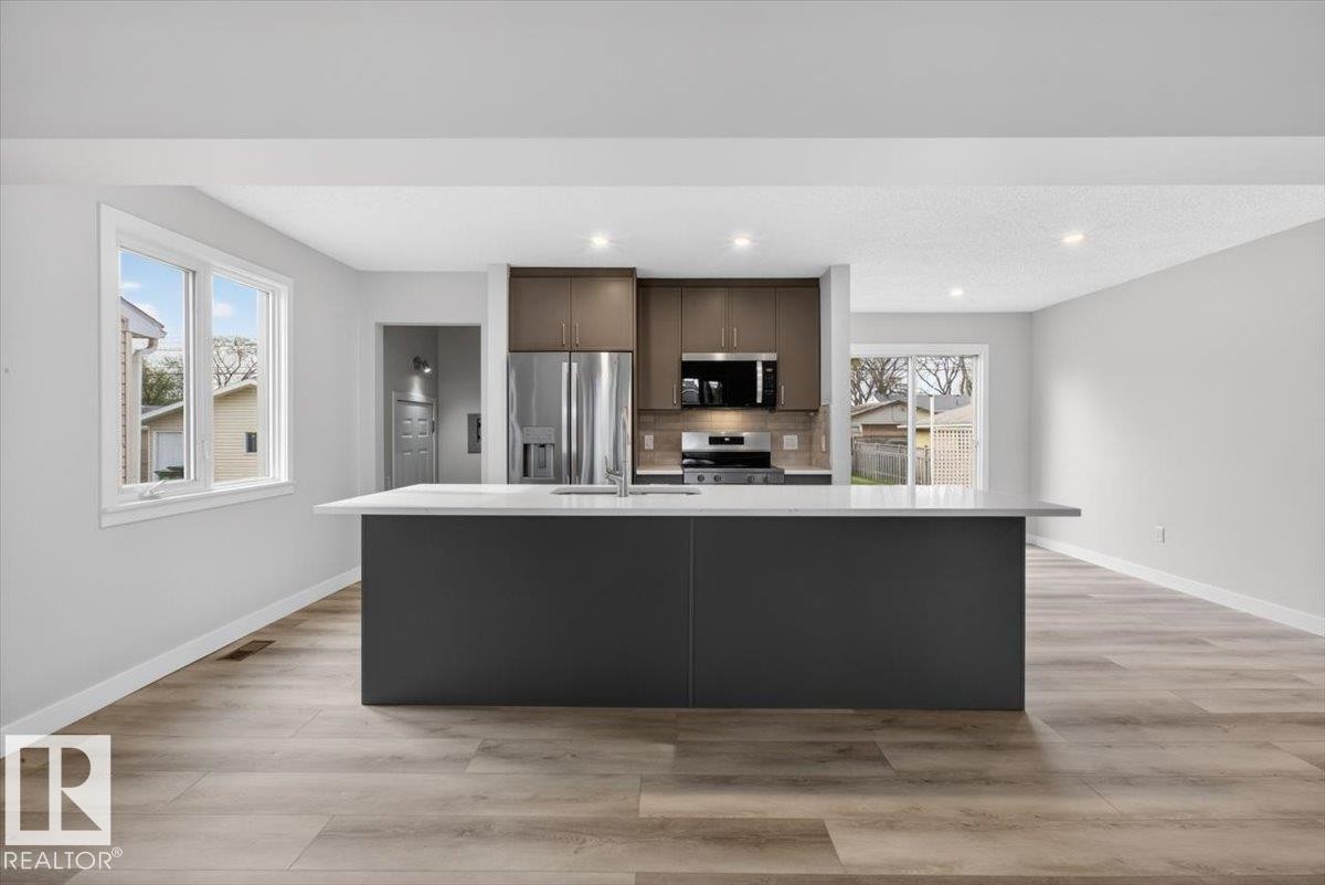 Modern kitchen featuring a central island with a light-colored countertop, stainless steel appliances, two-tone cabinetry, wood-finish flooring, and recessed lighting - 9723 65 Avenue Nw, Edmonton, AB