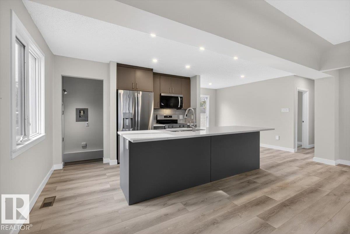 Modern kitchen featuring a central island with an integrated sink and gooseneck faucet - 9723 65 Avenue Nw, Edmonton, AB