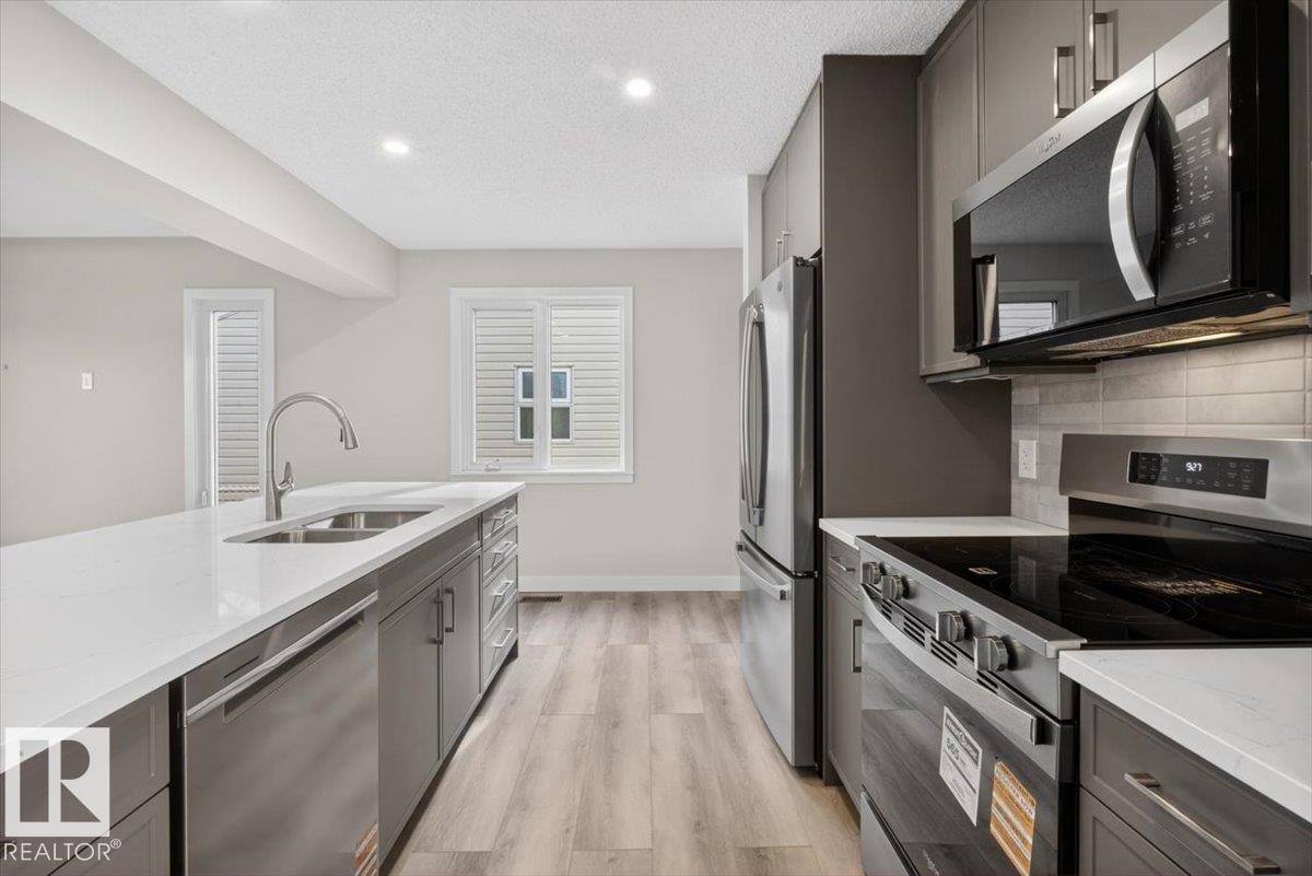 Contemporary kitchen featuring light wood-finish flooring, white countertops, stainless steel appliances, and sleek gray cabinetry - 9723 65 Avenue Nw, Edmonton, AB