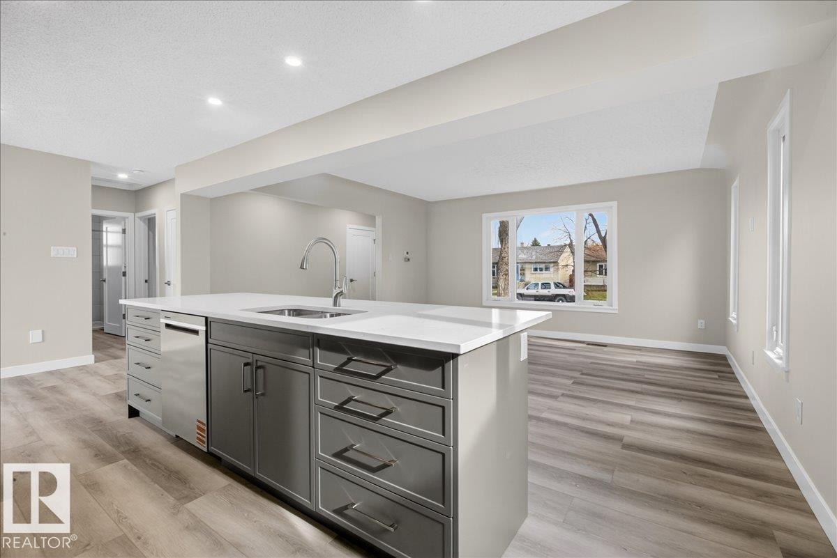 Kitchen island featuring gray cabinetry, a stainless steel sink with a high-arc faucet, and white countertops - 9723 65 Avenue Nw, Edmonton, AB