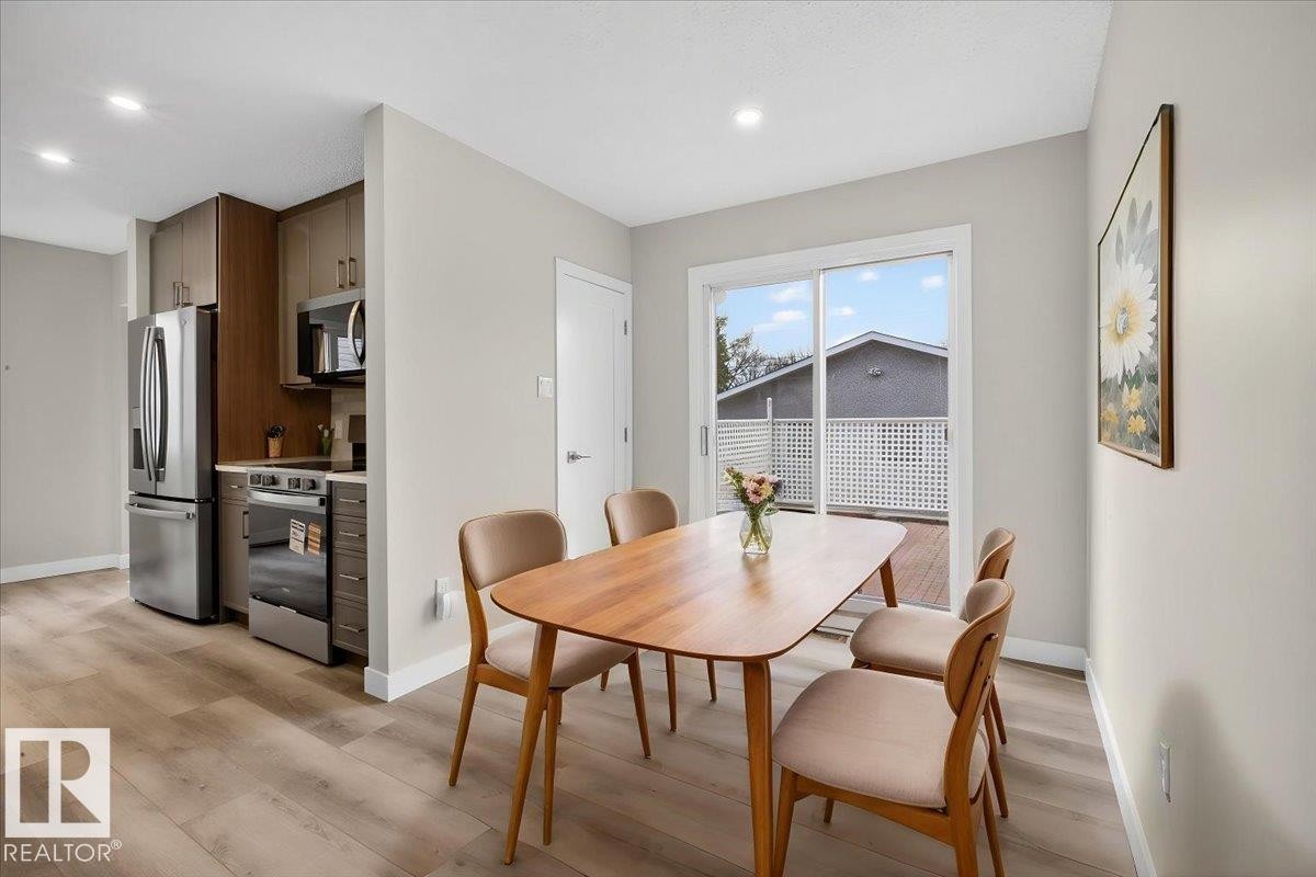 Open-concept dining area with wood-finish flooring, a sliding glass door leading to an outdoor deck, and recessed lighting - 9723 65 Avenue Nw, Edmonton, AB