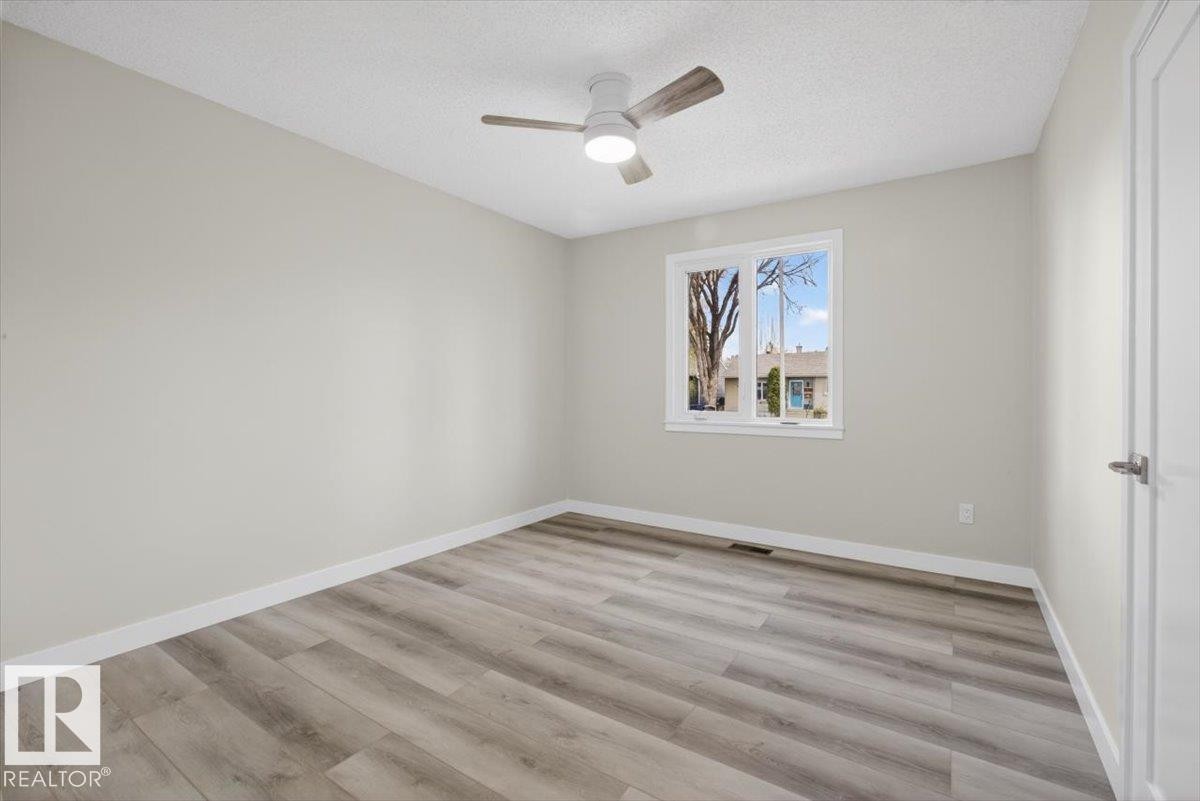 Spacious room featuring wood-finish flooring, a white trim baseboard, and light-colored walls - 9723 65 Avenue Nw, Edmonton, AB