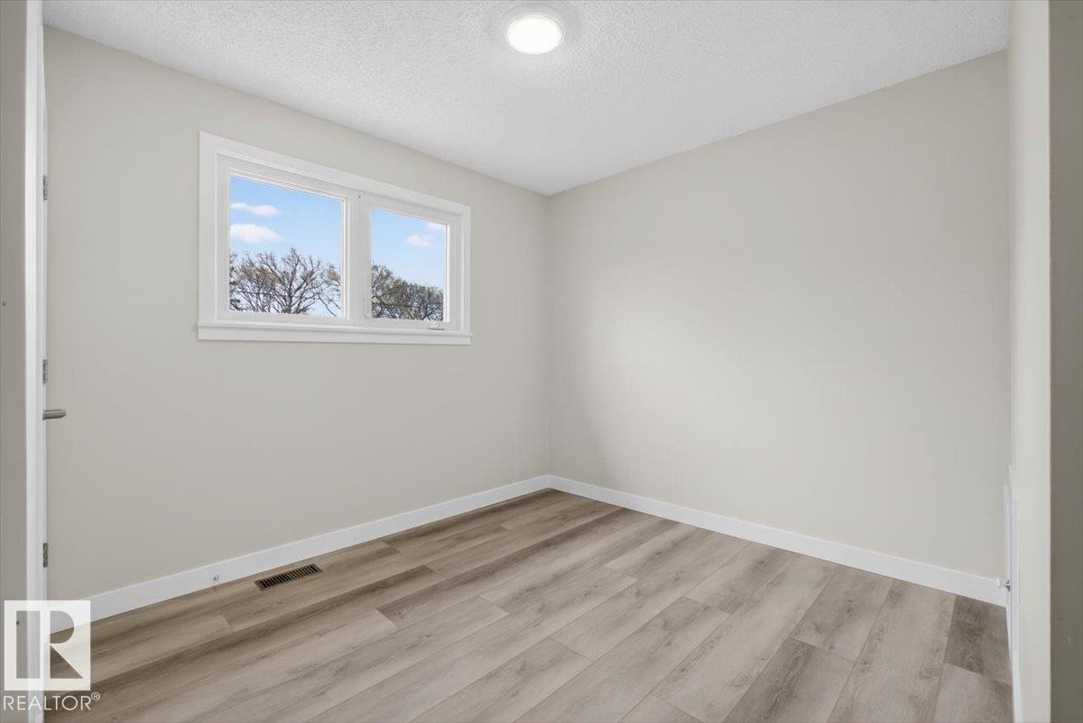 Bright room featuring a two-pane window, wood-finish flooring, light gray walls, white baseboards, and a flush-mounted ceiling light fixture - 9723 65 Avenue Nw, Edmonton, AB
