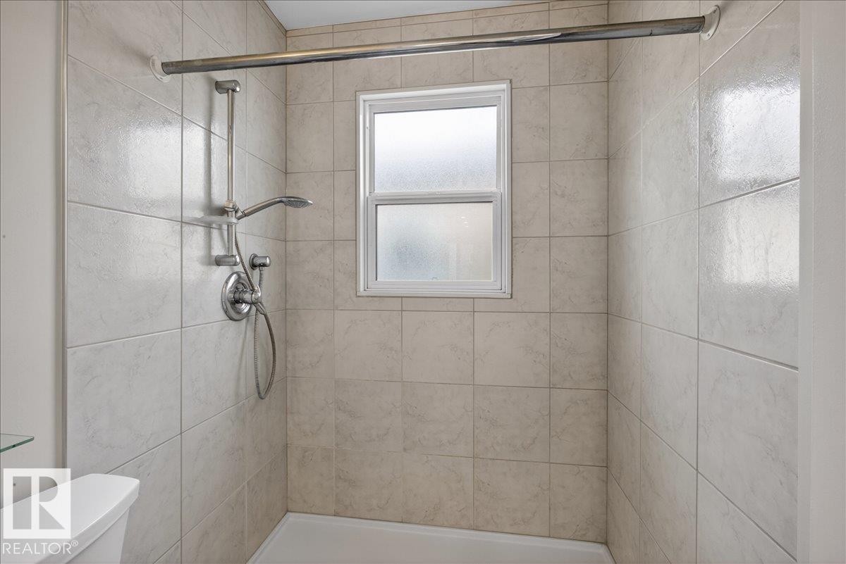 Shower enclosure with light-toned ceramic tile walls, a frosted window, and a chrome shower fixture - 9723 65 Avenue Nw, Edmonton, AB