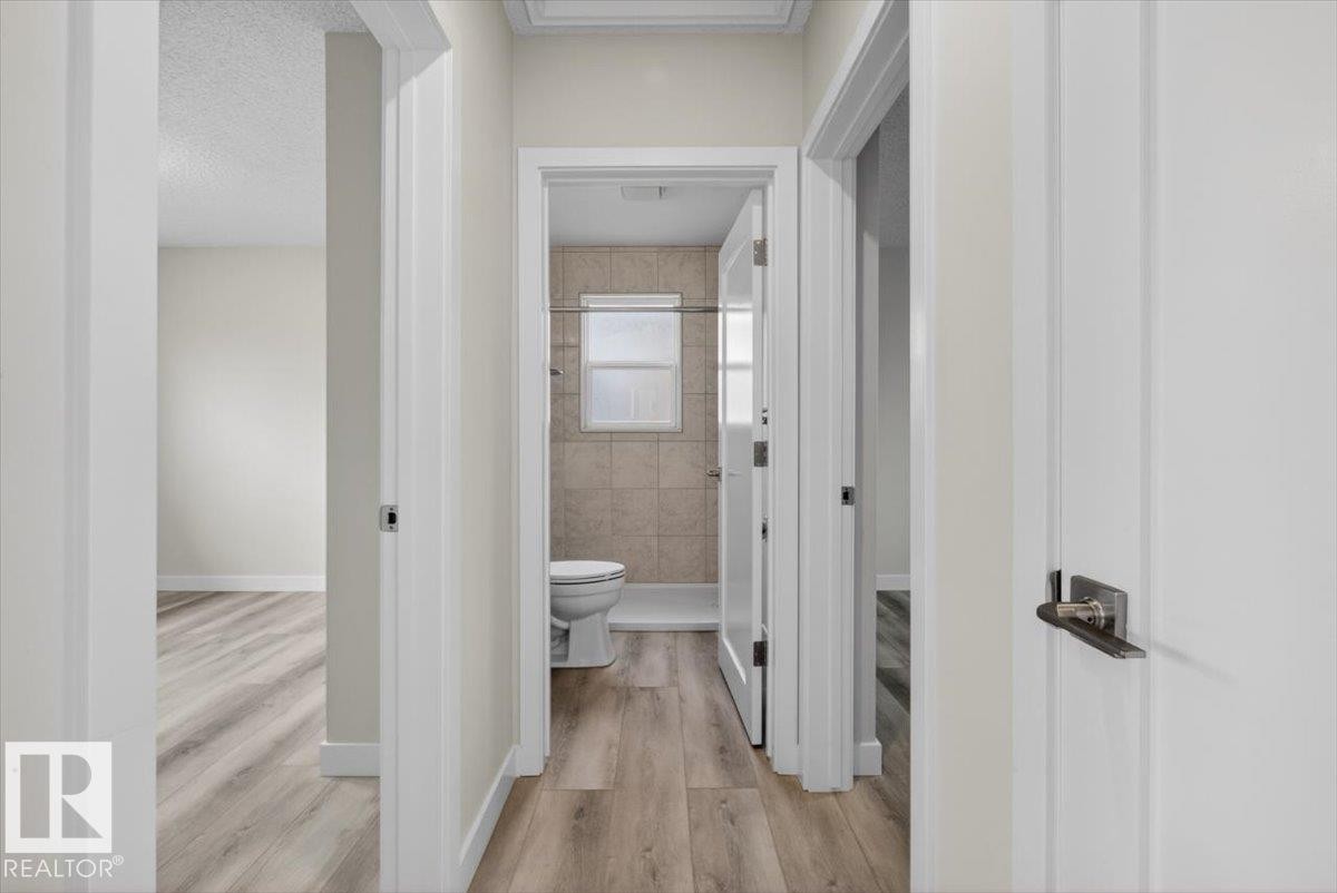 Hallway featuring light wood-finish flooring, white paneled doors, and contemporary door hardware - 9723 65 Avenue Nw, Edmonton, AB