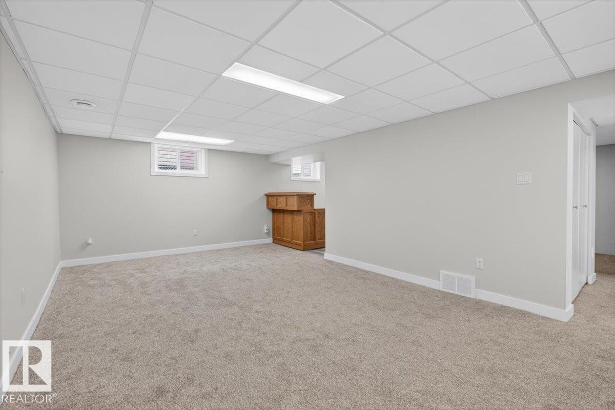 Spacious room featuring neutral carpeting, light gray walls, a drop ceiling with recessed lighting, and a built-in wooden cabinet - 9723 65 Avenue Nw, Edmonton, AB