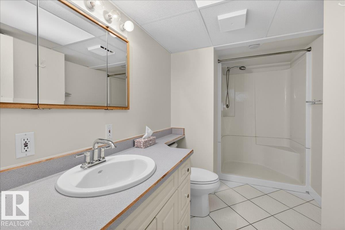 Bathroom featuring a white oval undermount sink, dual-handle faucet, and a large medicine cabinet with integrated lighting - 9723 65 Avenue Nw, Edmonton, AB
