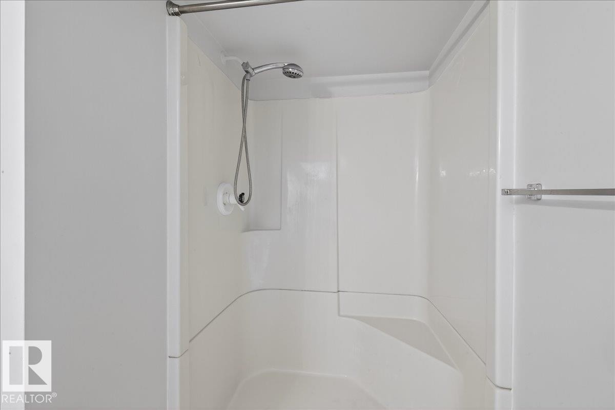 White fiberglass shower enclosure with an integrated seat and a handheld showerhead - 9723 65 Avenue Nw, Edmonton, AB