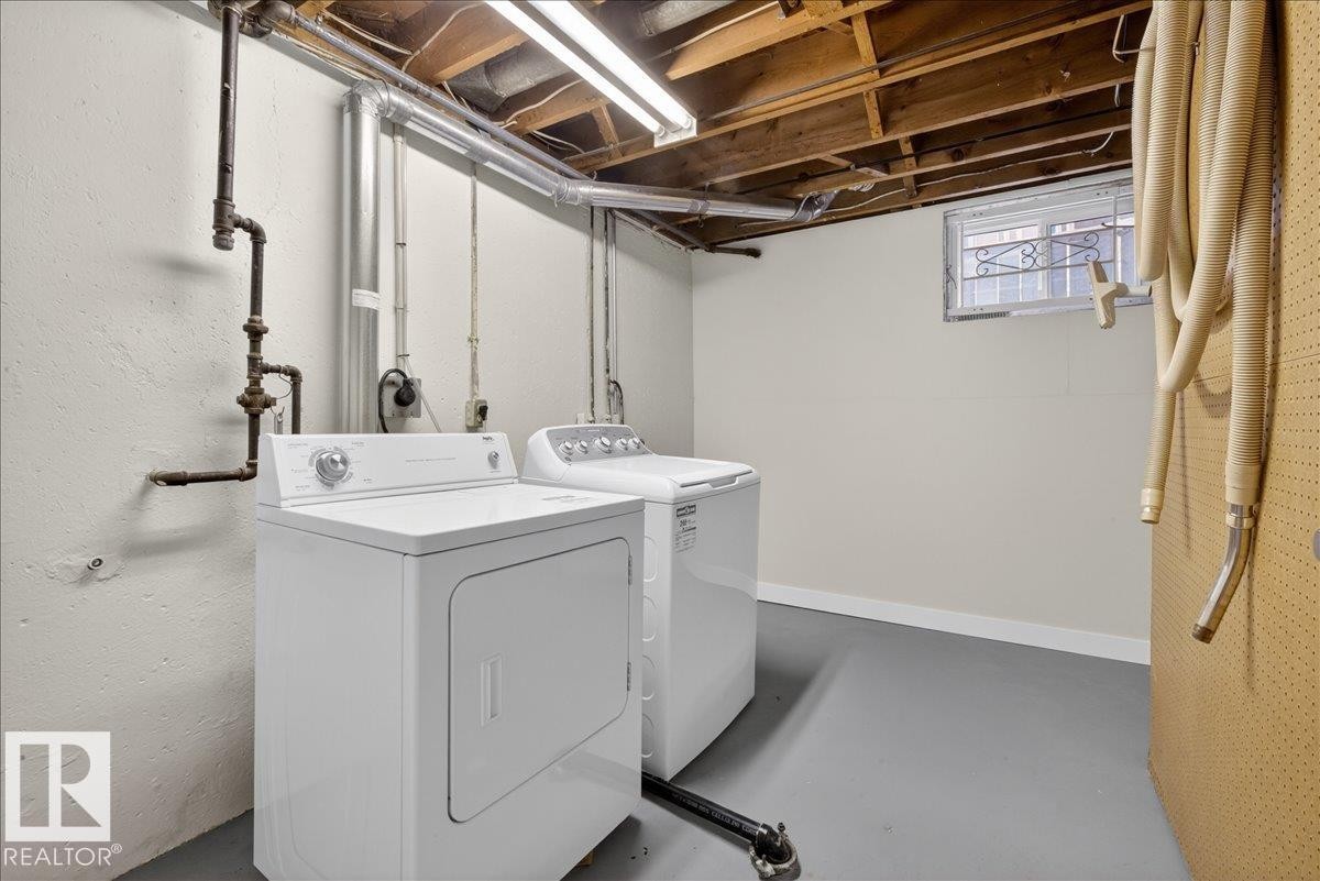 Dedicated laundry area featuring a washer and dryer, exposed ceiling joists, and a painted concrete floor - 9723 65 Avenue Nw, Edmonton, AB