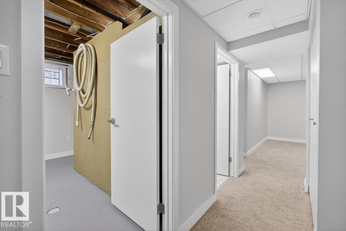 Lower level featuring a finished hallway with neutral carpeting, white trim, and a drop ceiling with recessed lighting - 9723 65 Avenue Nw, Edmonton, AB