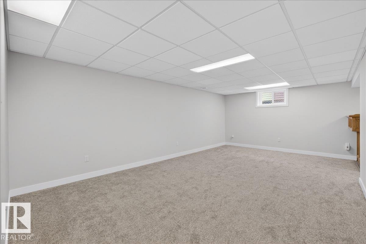 Spacious room featuring light gray carpeting, white baseboards, and a drop ceiling with recessed lighting - 9723 65 Avenue Nw, Edmonton, AB