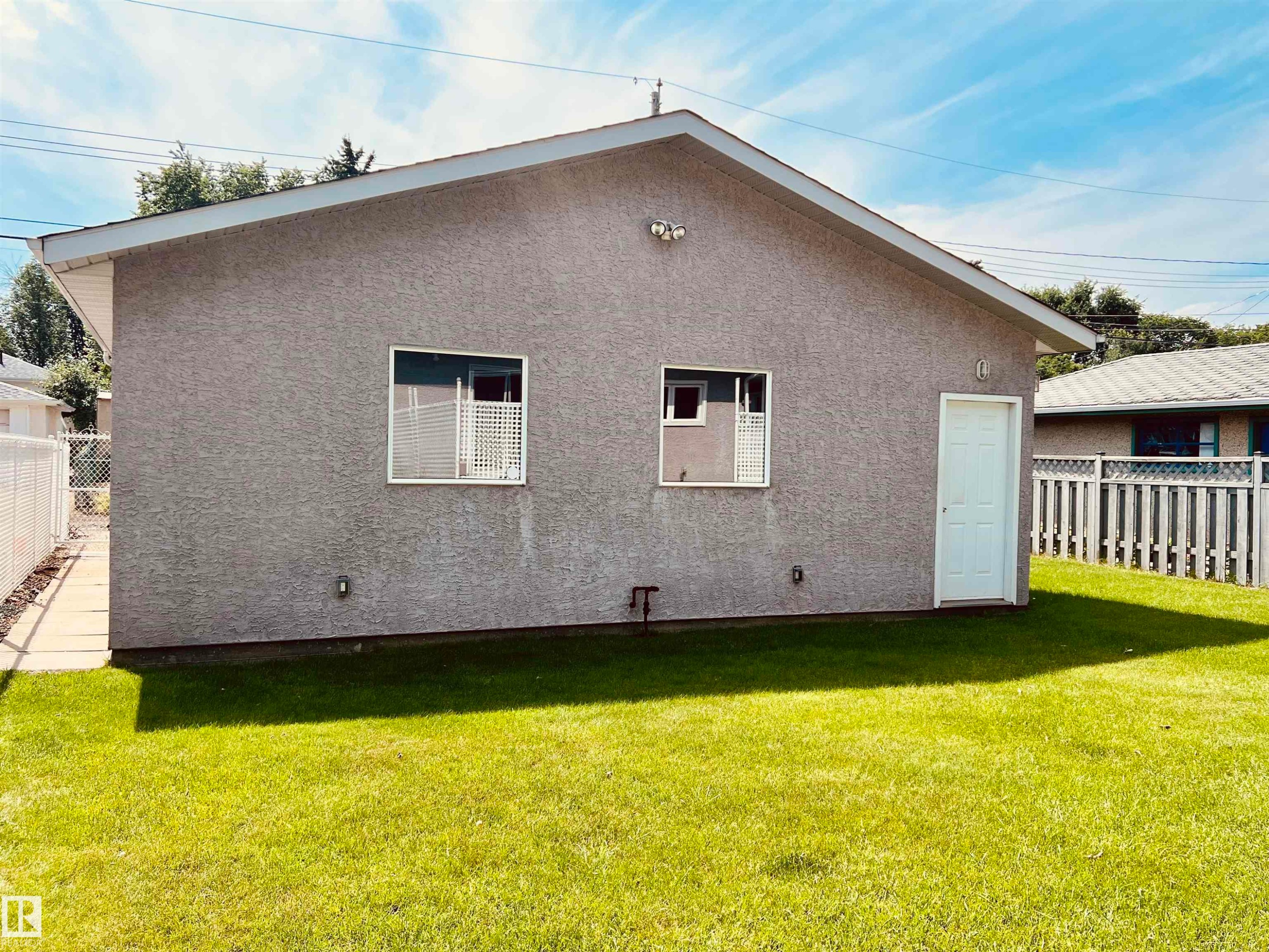 Exterior featuring a stucco finish, a pitched roof, and a white entry door - 9723 65 Avenue Nw, Edmonton, AB