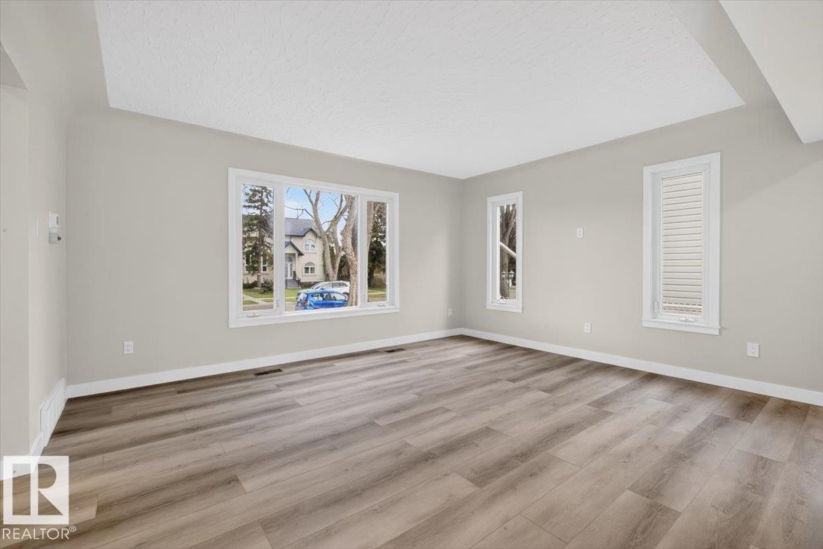 Spacious room featuring light-toned walls and wood-finish flooring - 9723 65 Avenue Nw, Edmonton, AB