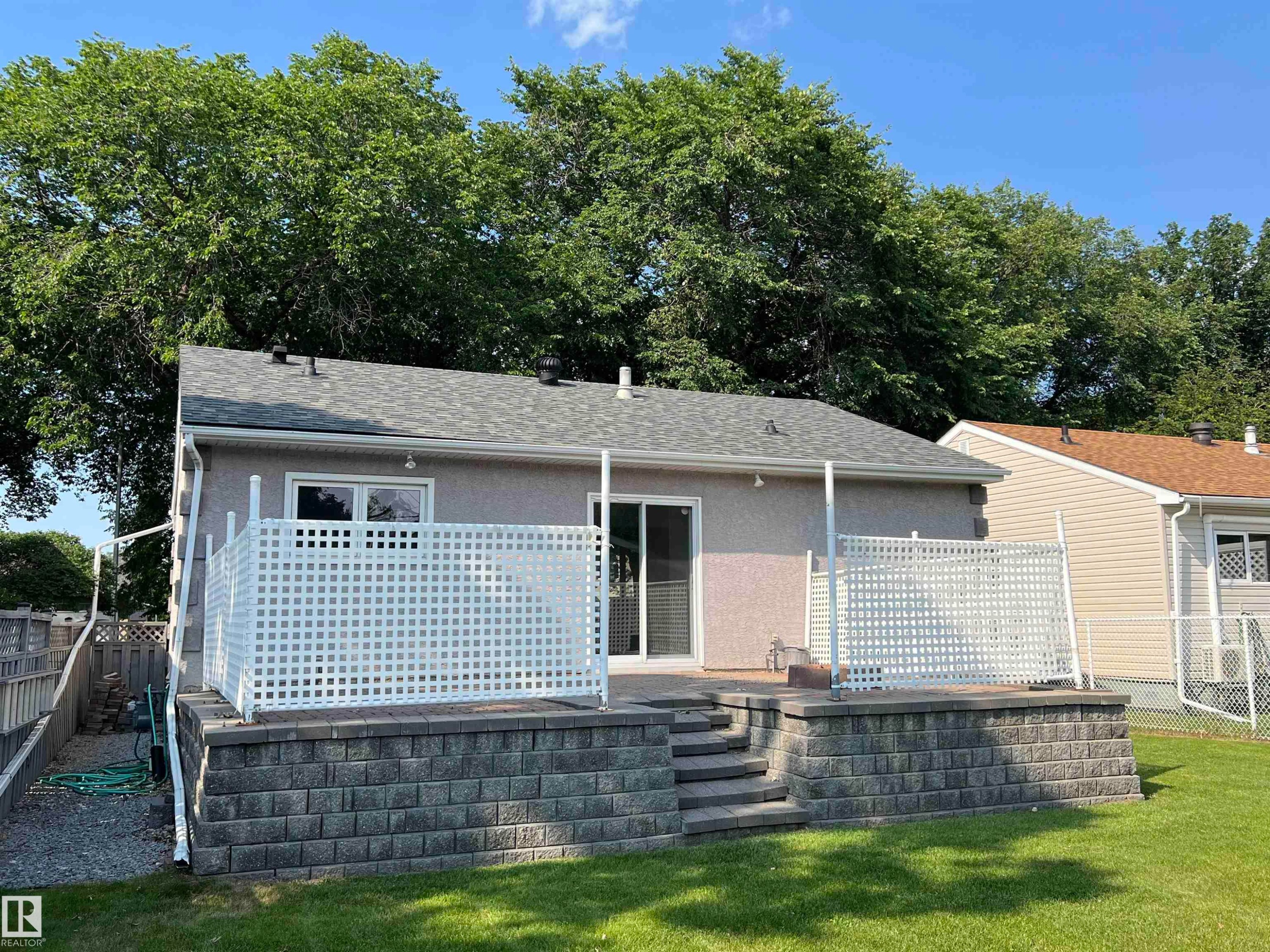 Private outdoor patio featuring a privacy lattice, block retaining wall, and a staircase to the yard - 9723 65 Avenue Nw, Edmonton, AB