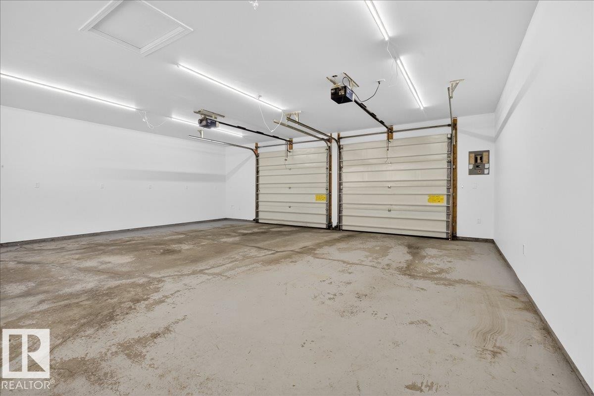 Two-car garage featuring segmented overhead doors with openers, exposed ceiling joists, and fluorescent strip lighting - 9723 65 Avenue Nw, Edmonton, AB