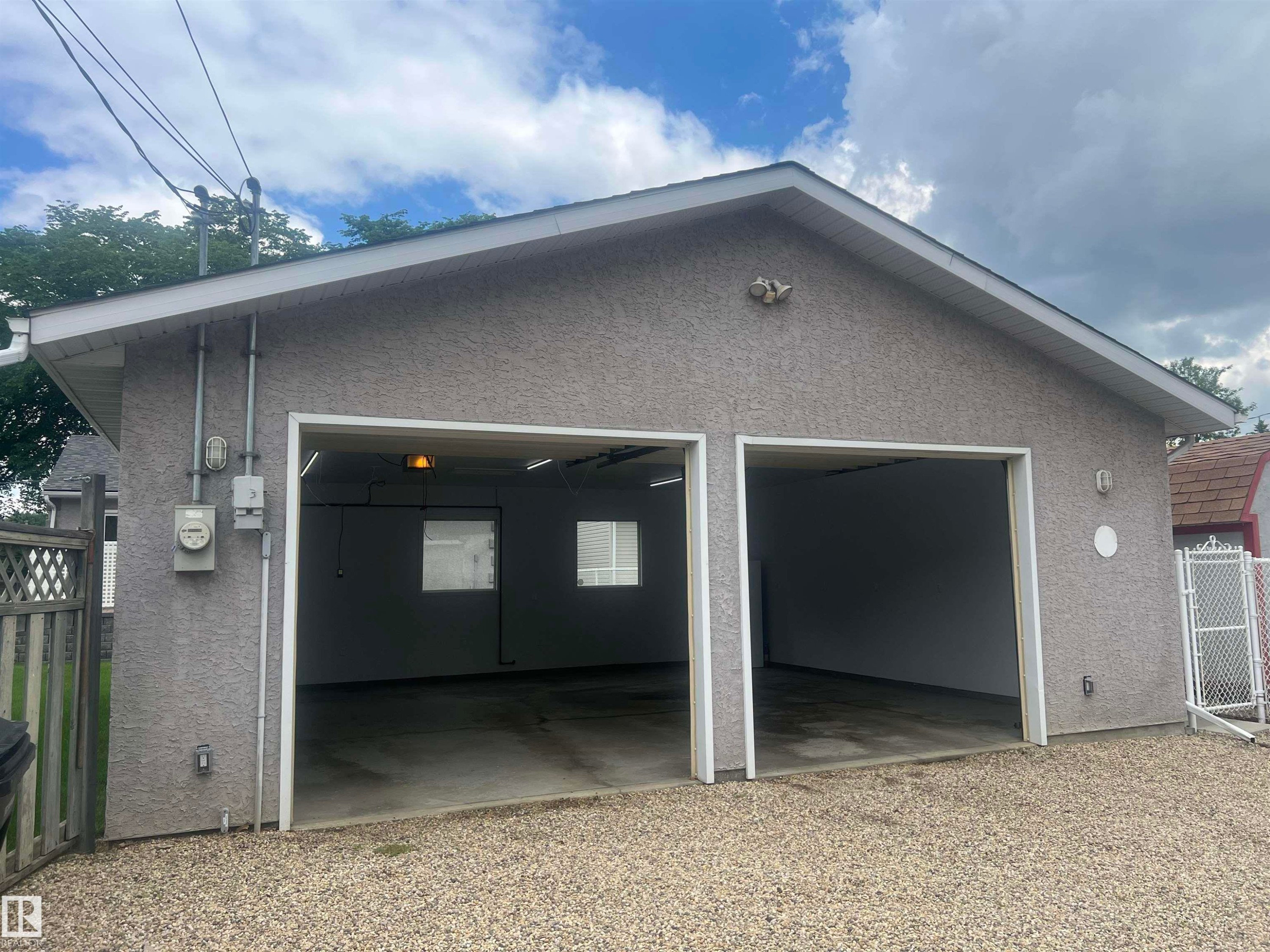 Two-car garage featuring a stucco exterior finish and a gravel driveway - 9723 65 Avenue Nw, Edmonton, AB