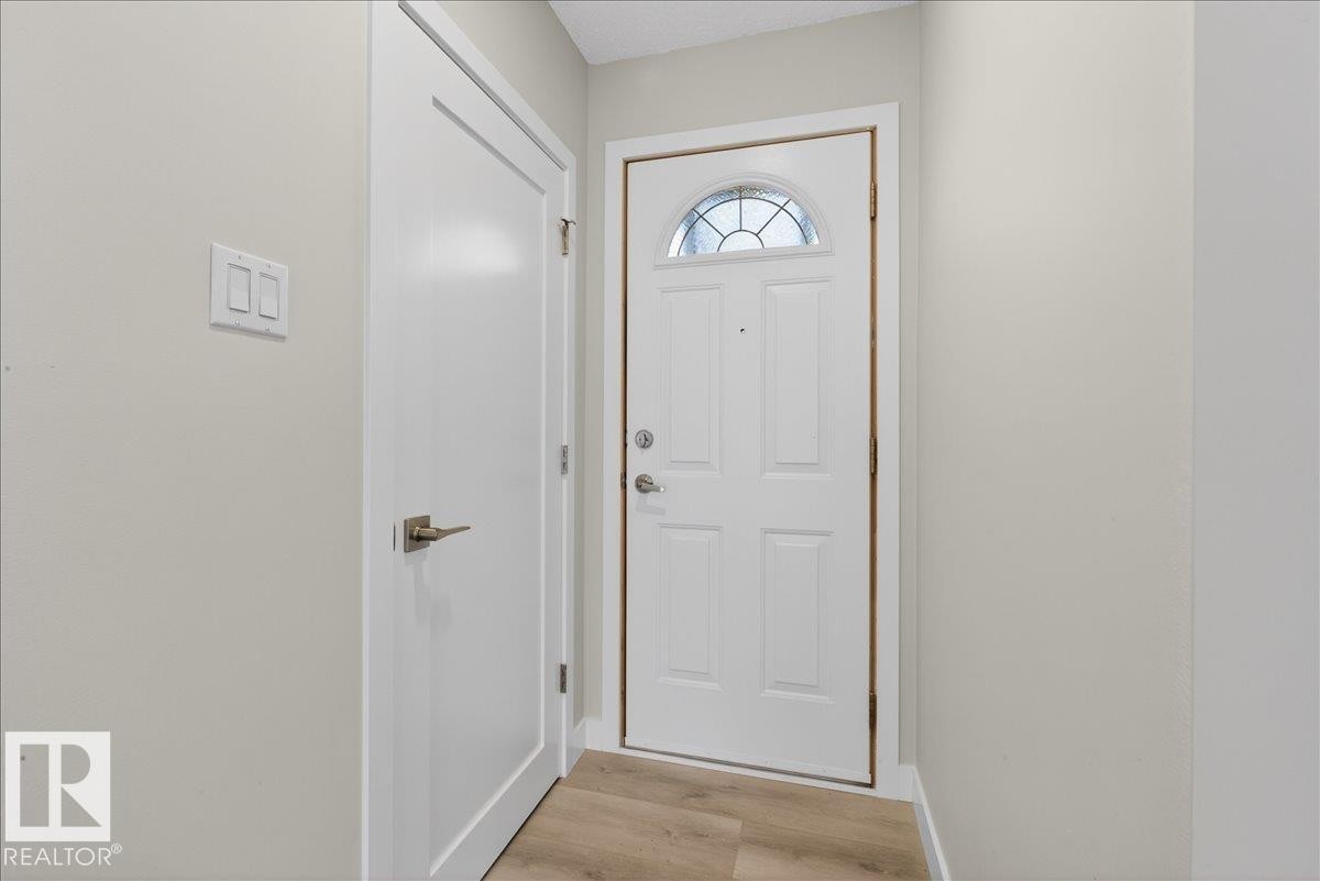 Entryway featuring a paneled white door with an arched glass insert, a second white door with brushed nickel hardware, light wood-finish flooring, and light-toned walls - 9723 65 Avenue Nw, Edmonton, AB