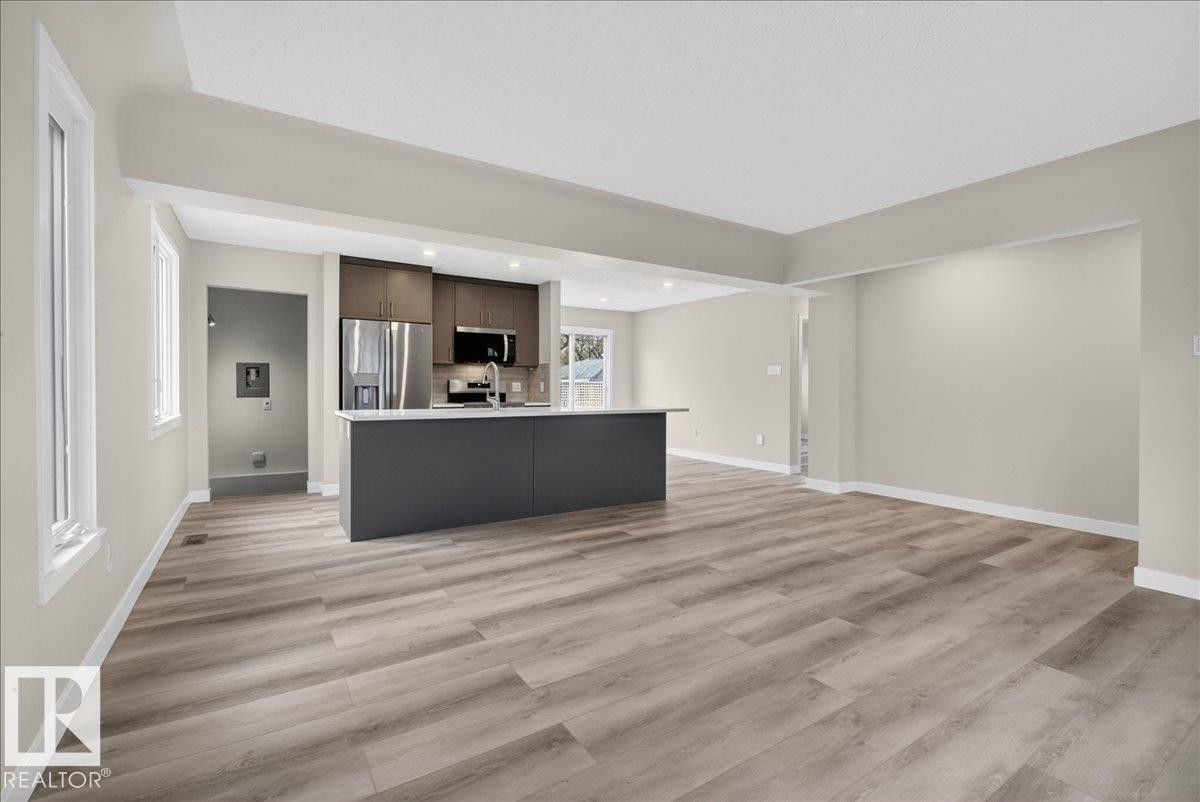 Expansive room featuring wood-finish flooring, a kitchen island with a light-toned countertop, and stainless steel appliances including a refrigerator, microwave, and range - 9723 65 Avenue Nw, Edmonton, AB