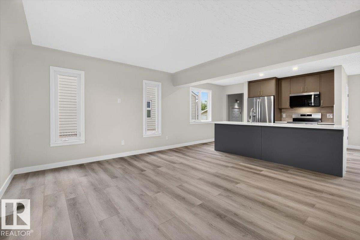 Open-concept living area featuring wood-finish flooring, light-toned walls, and a kitchen island with a white countertop - 9723 65 Avenue Nw, Edmonton, AB