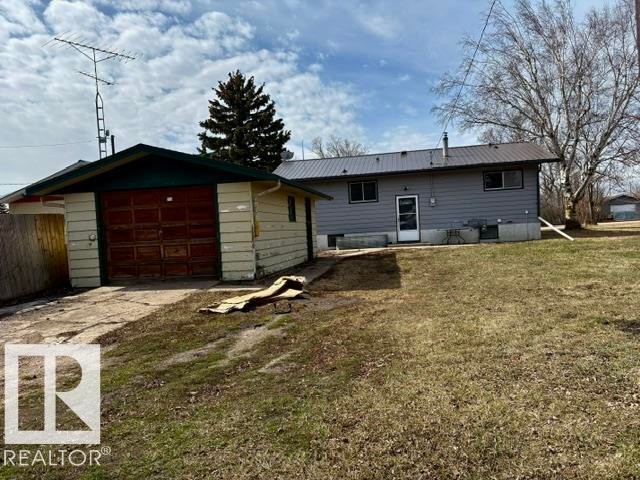 Detached garage with a paneled wood-finish door, metal roof, and adjacent gravel driveway - 5206 51Ave, Willingdon, AB - Outdoor With Exterior