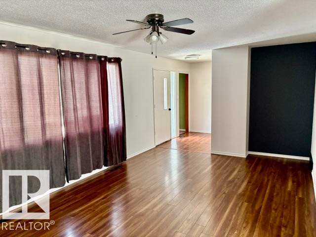 Spacious room featuring wood-finish flooring, a ceiling fan, and white walls with a contrasting accent wall - 5206 51Ave, Willingdon, AB - Indoor Photo Showing Other Room