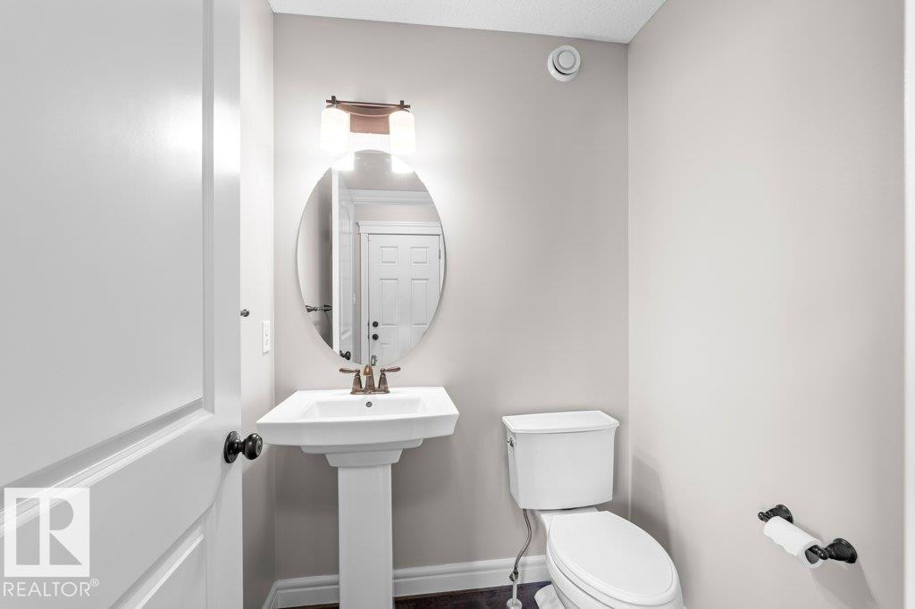 Pedestal sink with bronze-finish faucet, oval mirror, and overhead lighting fixture - 1627 167 Street Sw, Edmonton, AB - Indoor Photo Showing Bathroom
