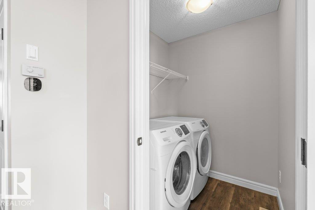 Dedicated laundry area featuring a white front-load washer and dryer set, wire shelving, and wood-finish flooring - 1627 167 Street Sw, Edmonton, AB - Indoor Photo Showing Laundry Room