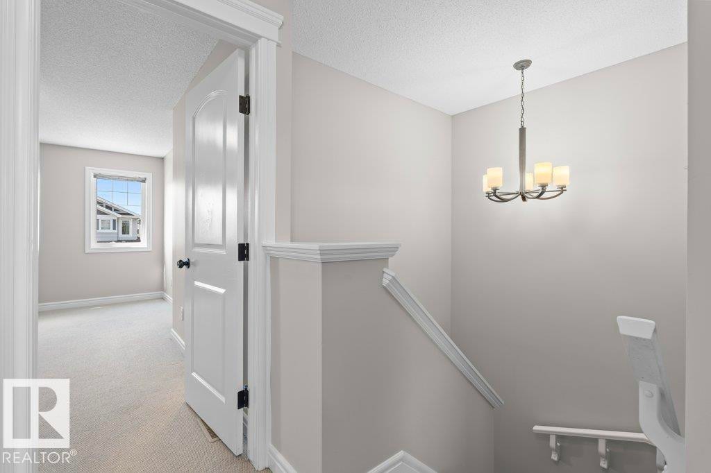 Contemporary chandelier illuminating the stairwell, featuring a neutral color palette, white trim work, and a paneled interior door - 1627 167 Street Sw, Edmonton, AB - Indoor Photo Showing Other Room