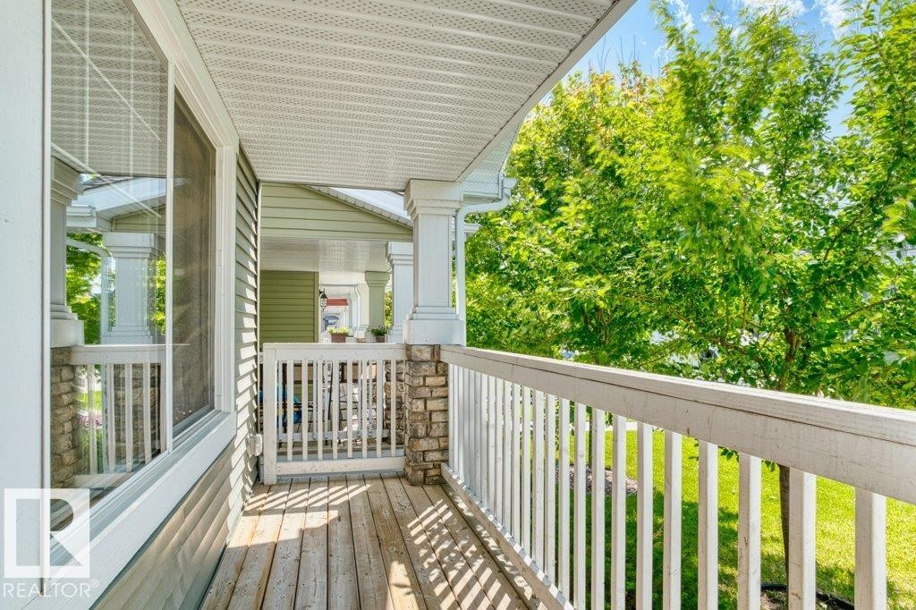 Covered porch featuring wood-finish flooring, white railing, stone column accents, and vinyl siding - 1627 167 Street Sw, Edmonton, AB - Outdoor With Exterior