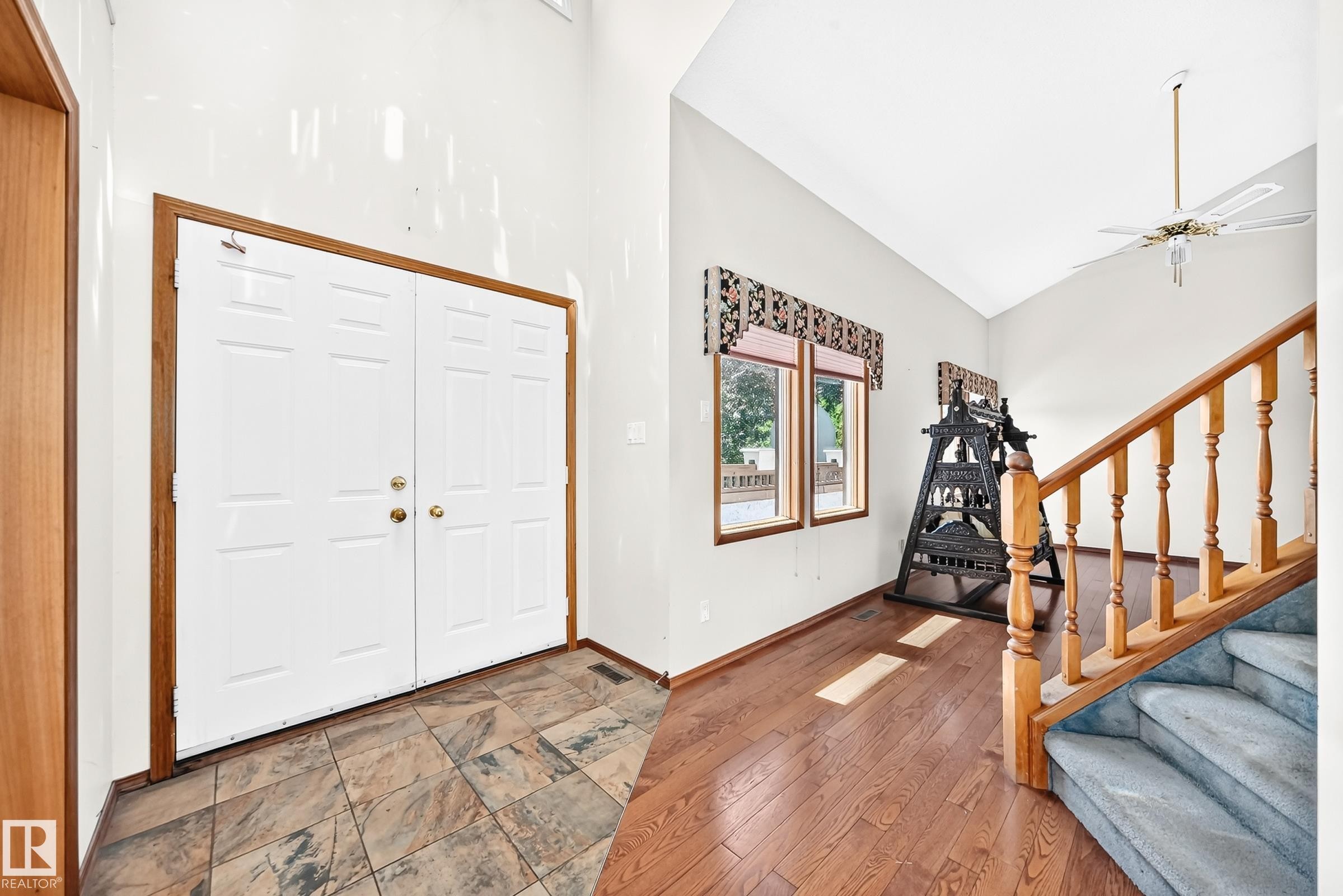 Entryway featuring double panel doors with brass hardware, slate tile flooring, wood-finish flooring, a wood staircase with carpeted treads, and vaulted ceilings - 4208 Ramsay Road Nw, Edmonton, AB - Indoor Photo Showing Other Room