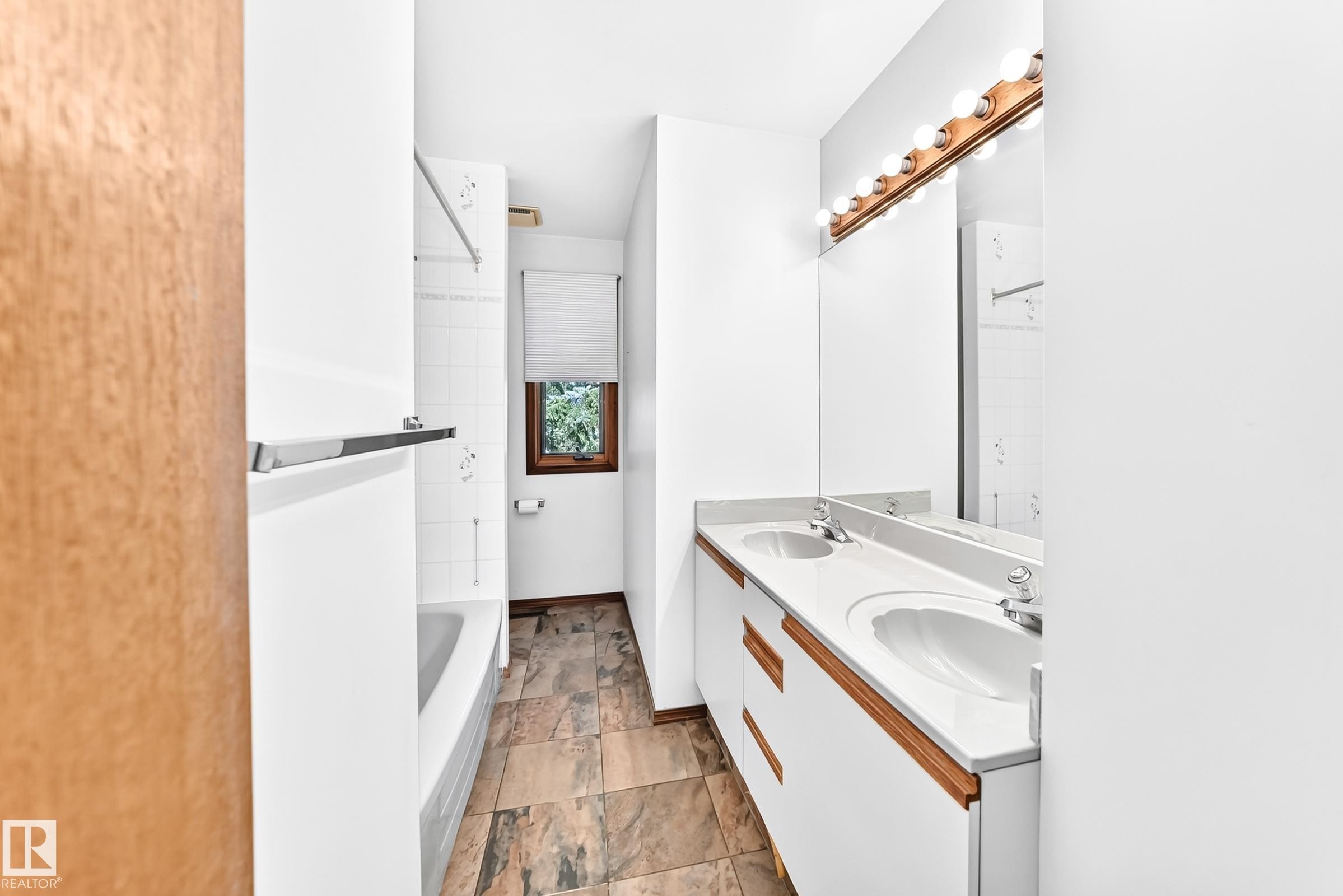 Bathroom featuring a dual vanity with integrated sinks, a wood-trimmed mirror, and a white bathtub with tile surround - 4208 Ramsay Road Nw, Edmonton, AB - Indoor Photo Showing Bathroom