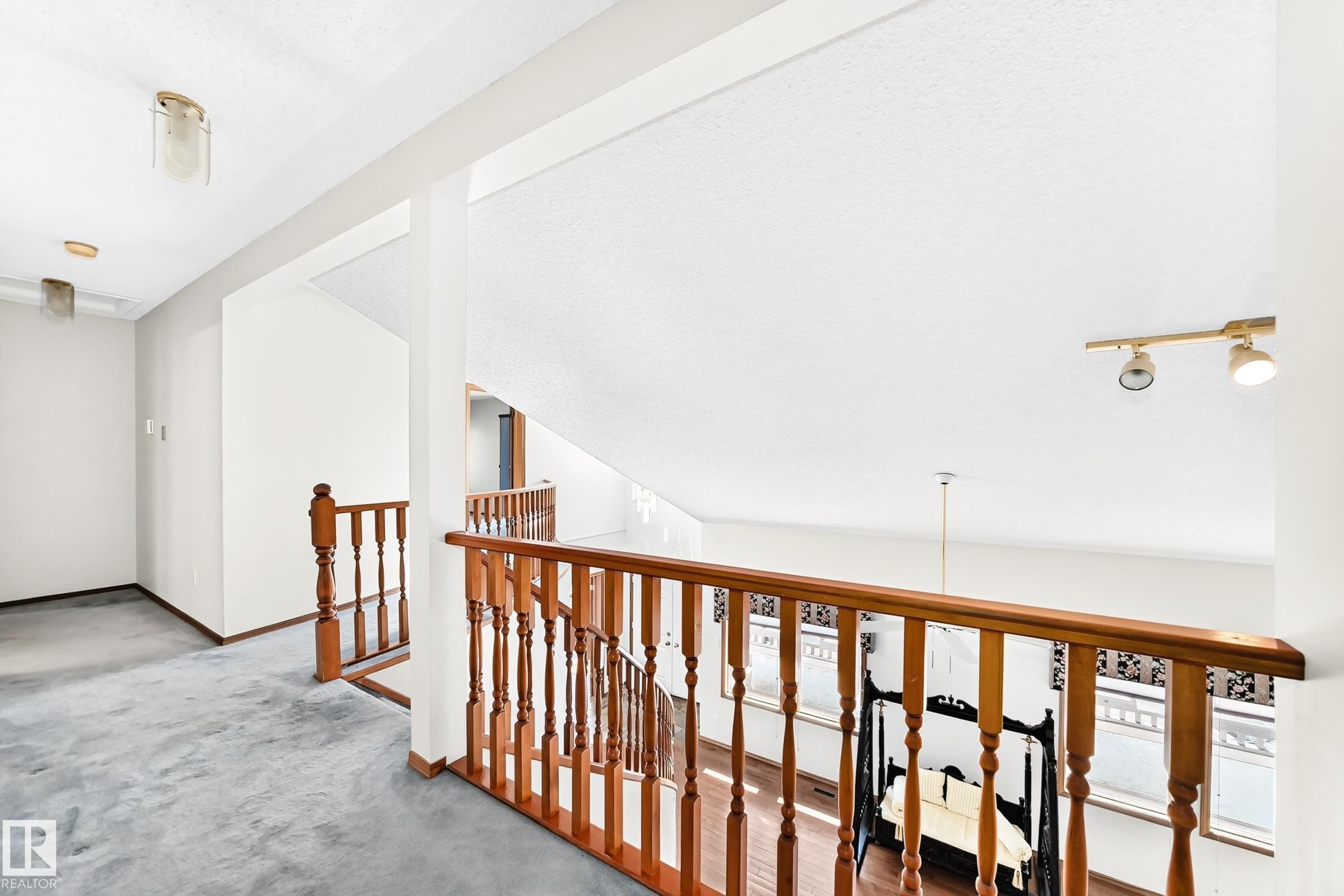 Upper-level landing featuring hardwood banister and spindles, track lighting, and a high ceiling - 4208 Ramsay Road Nw, Edmonton, AB - Indoor Photo Showing Other Room