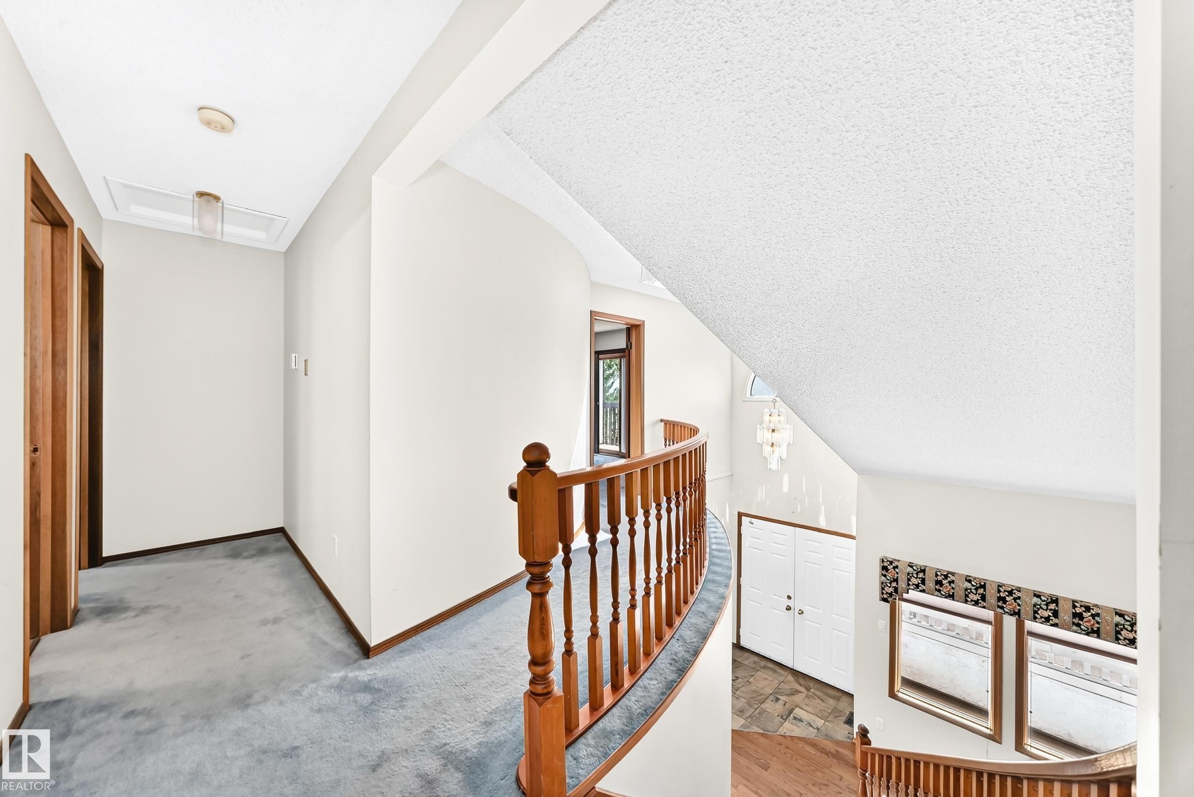 Curved wooden banister overlooking a lower level, featuring a light blue carpeted hallway with wood-finish doors, and a skylight - 4208 Ramsay Road Nw, Edmonton, AB - Indoor Photo Showing Other Room