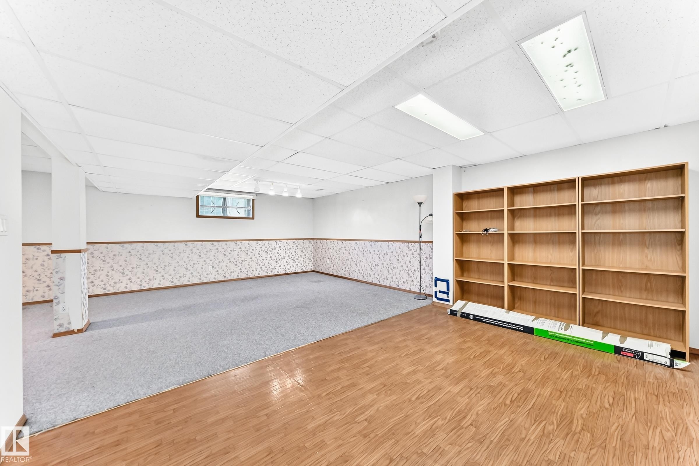 Spacious room featuring wood-finish flooring, light grey carpeting, built-in shelving, and a drop ceiling with recessed lighting - 4208 Ramsay Road Nw, Edmonton, AB - Indoor Photo Showing Other Room