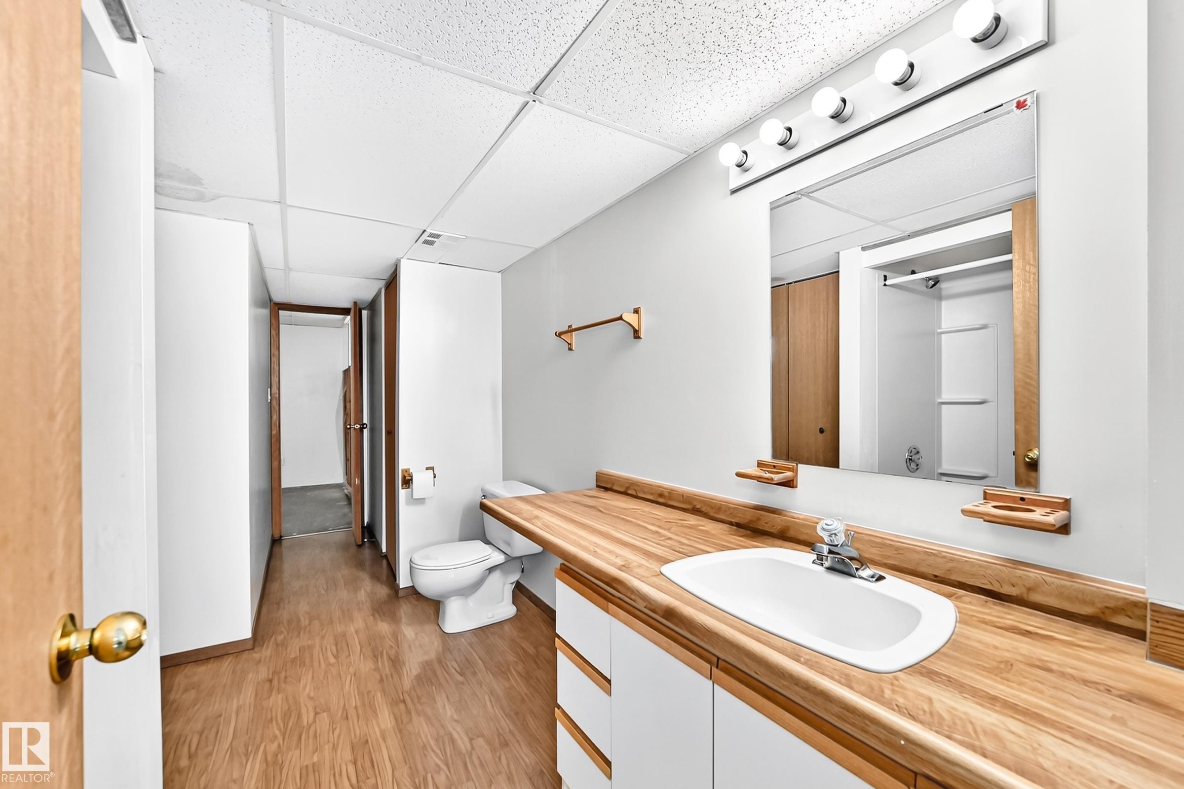 Bathroom featuring a wood-finish vanity countertop with an integrated sink, white cabinetry, and a large wall-mounted mirror with overhead vanity lighting - 4208 Ramsay Road Nw, Edmonton, AB - Indoor Photo Showing Bathroom