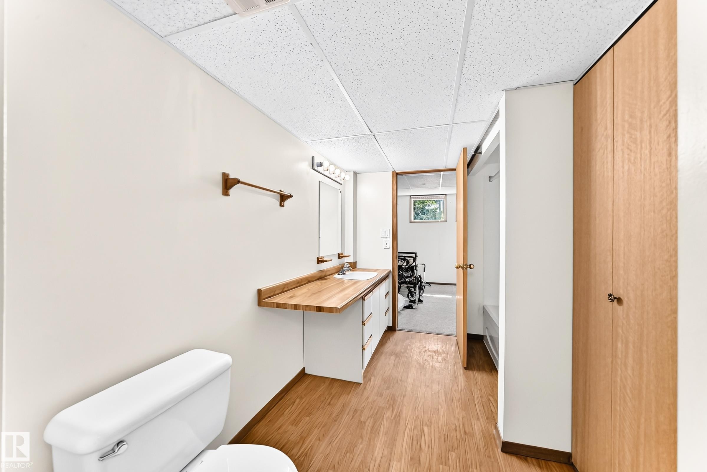 Bathroom featuring wood-finish flooring, a white toilet, a vanity with a wood-finish countertop and single sink, and a mirrored medicine cabinet with vanity lighting - 4208 Ramsay Road Nw, Edmonton, AB - Indoor